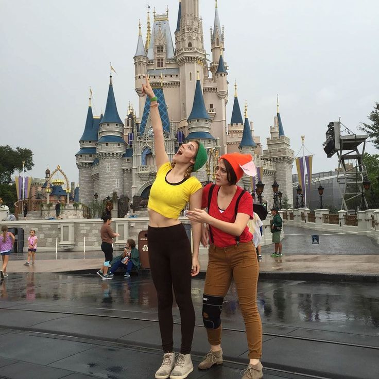 two women standing in front of a castle with their arms up to the sky and one holding an umbrella