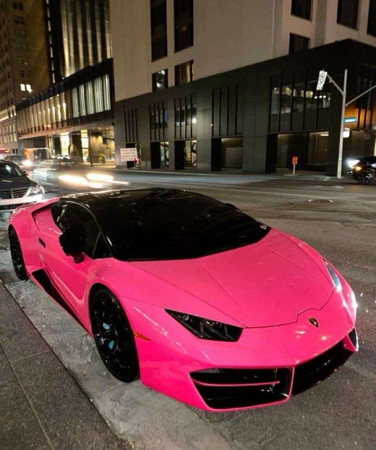 a pink sports car is parked on the side of the road in front of a building