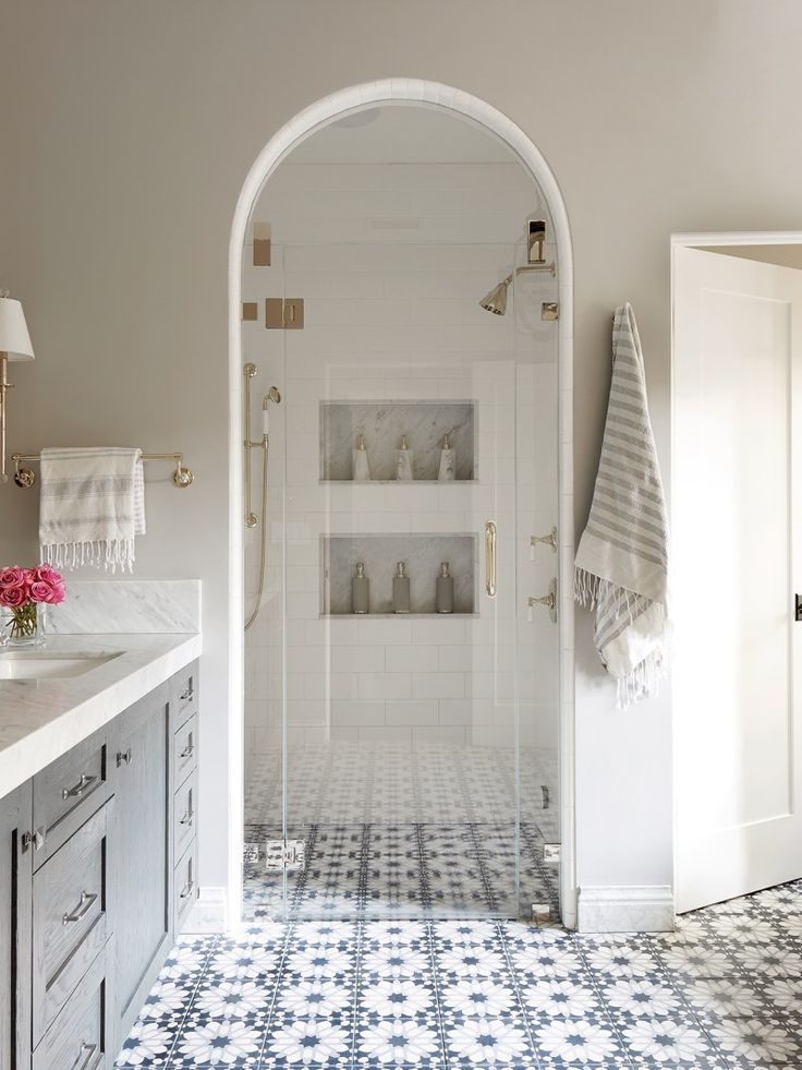 a white and blue tiled bathroom with an arched doorway leading into the shower area that has shelving units on either side