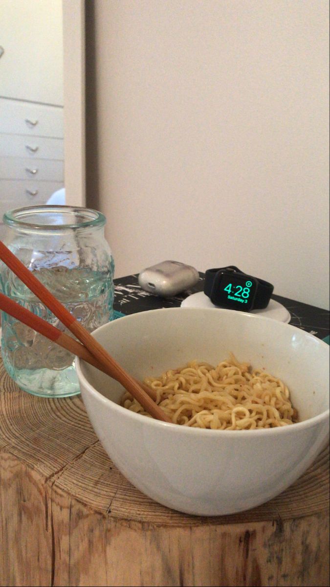 a bowl of noodles and chopsticks on a wooden table in front of a glass jar