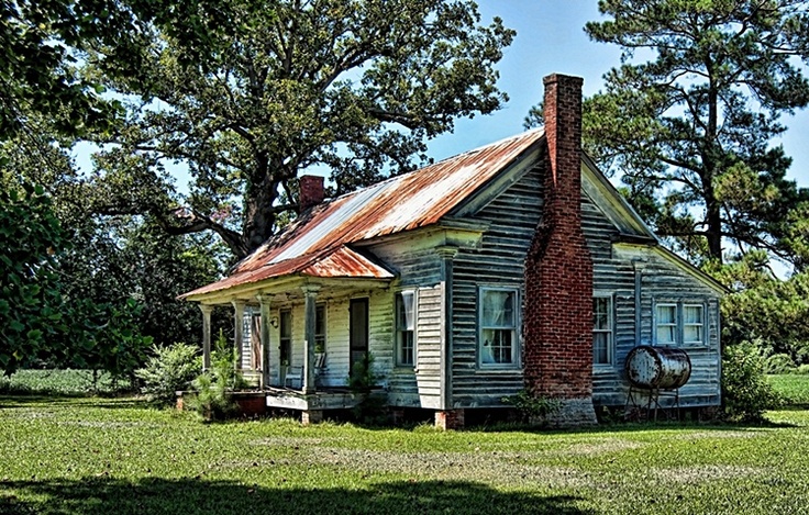 an old run down house in the middle of a grassy field with trees around it