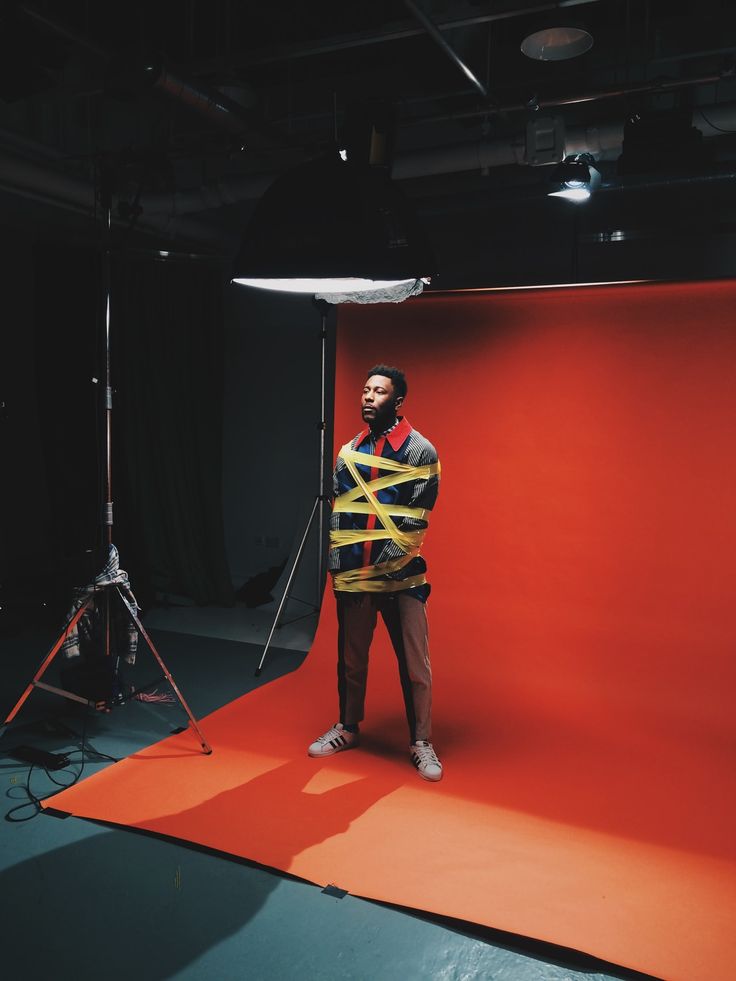 a man standing in front of a red backdrop with an orange and yellow striped jacket