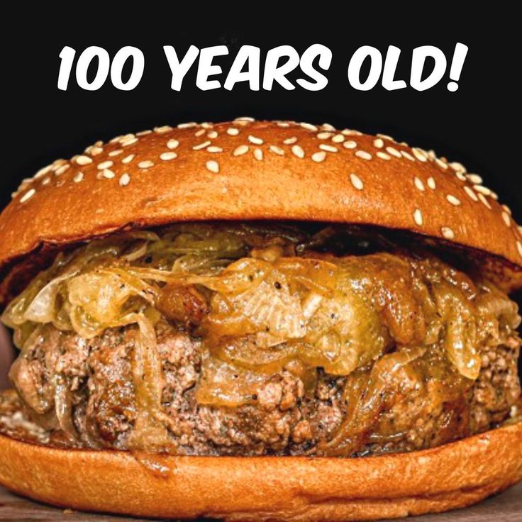 a large hamburger with onions and cheese on it, in front of a black background that says 100 years old