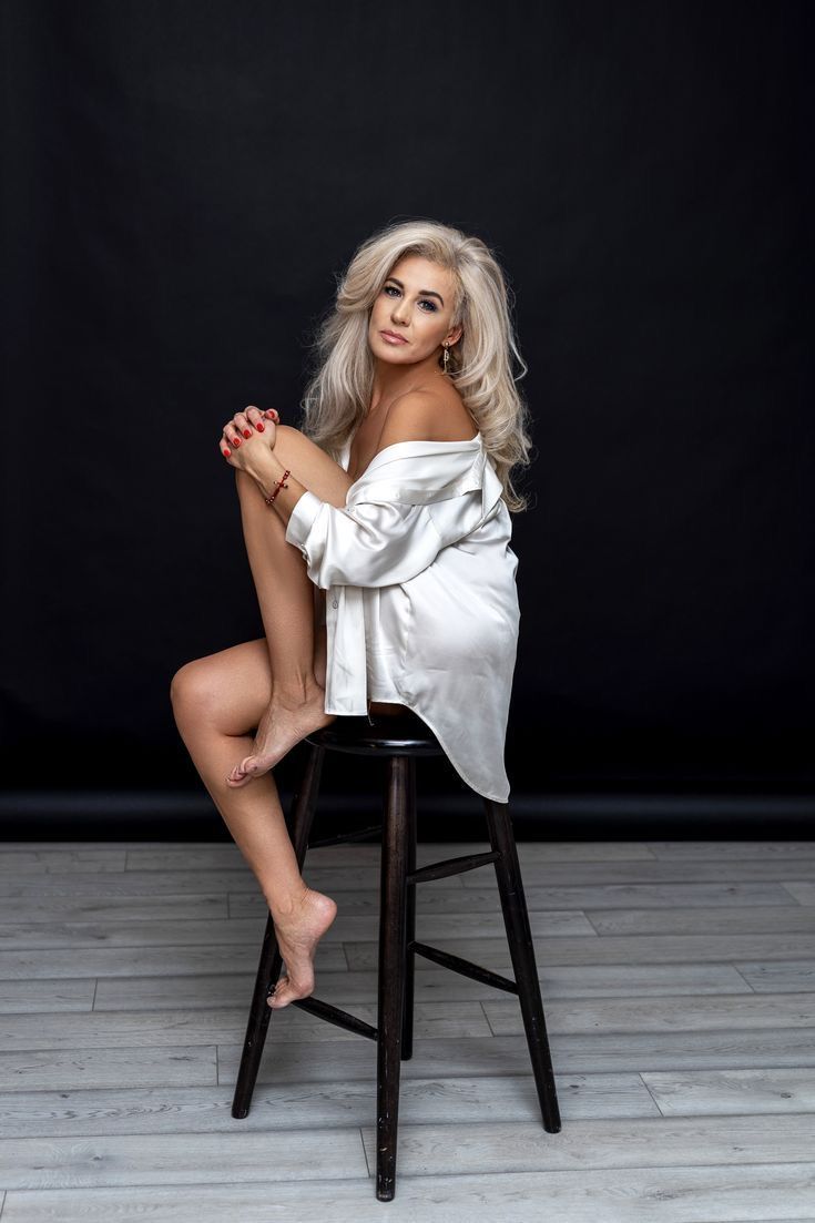 a woman sitting on top of a wooden chair in front of a black background with her legs crossed