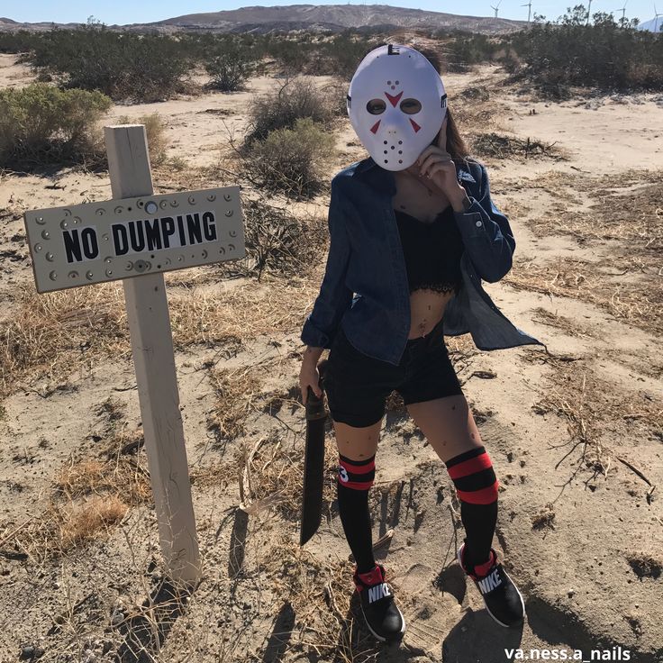 a woman wearing a mask standing next to a no dumping sign in the middle of nowhere