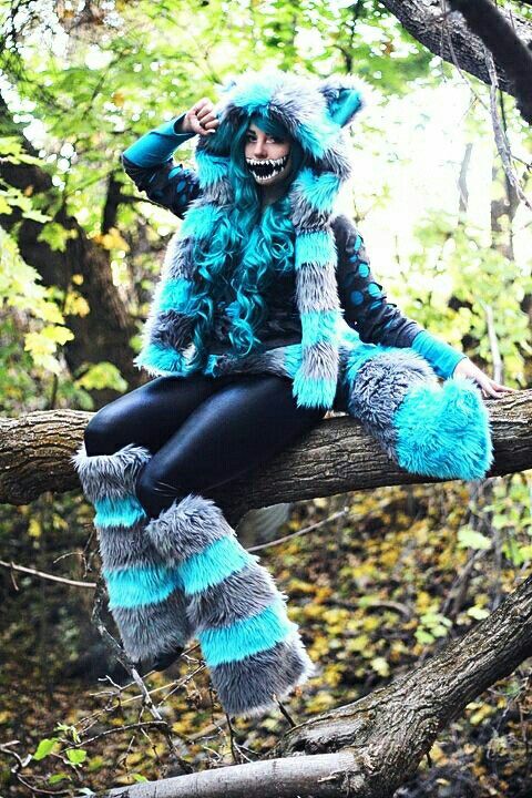 a woman sitting on top of a tree branch wearing blue and grey furry animal costumes