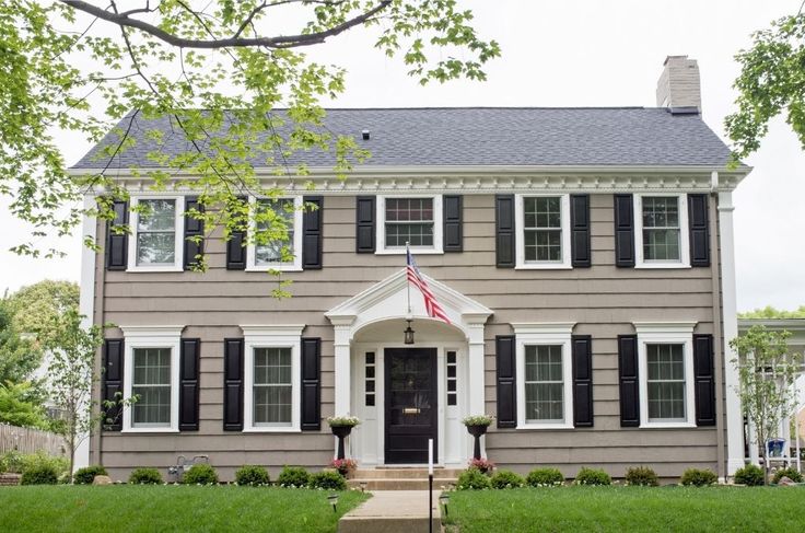 a large gray house with black shutters and an american flag on the front door