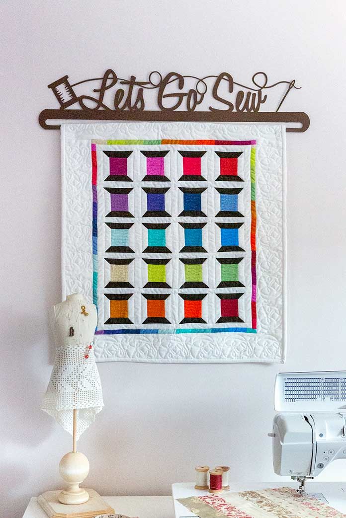 a sewing machine sitting on top of a white table next to a wall hanging quilt