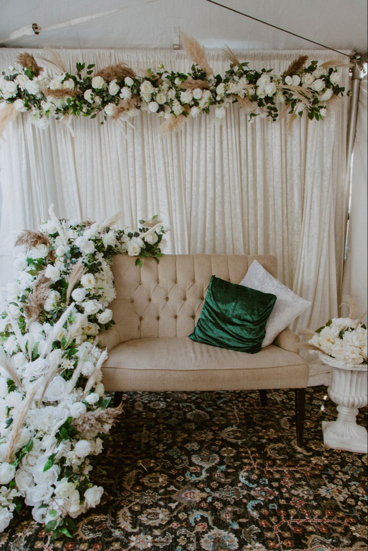 a couch sitting in front of a white curtain covered wall with flowers and greenery