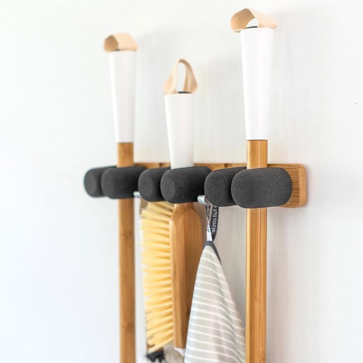 three wooden hooks holding towels and other items on a white wall next to a mirror