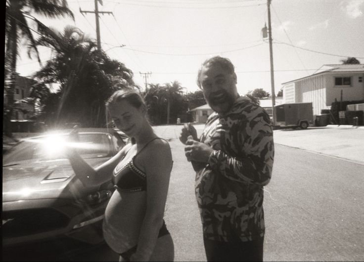 a man and woman standing next to each other in front of a car on the street