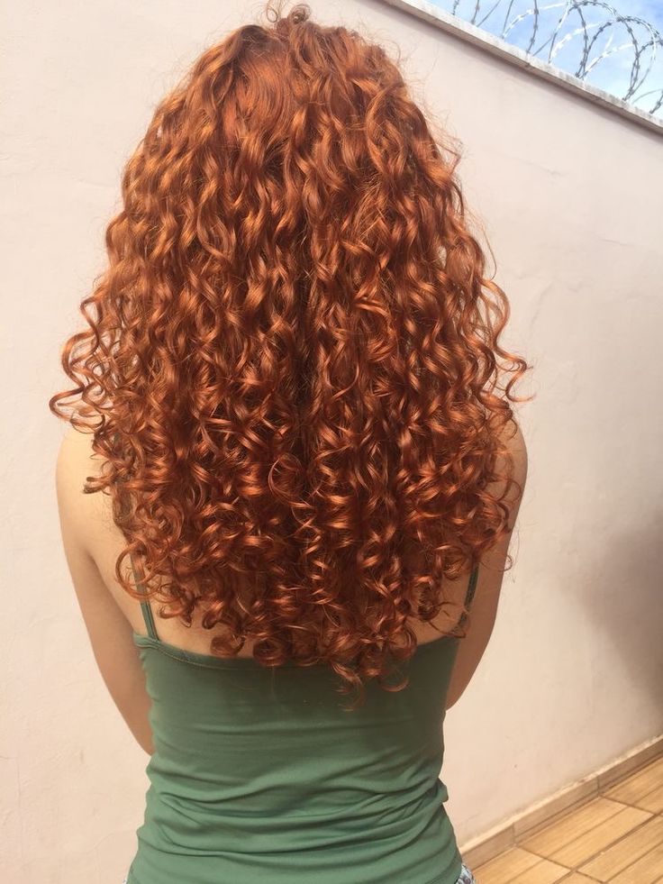 the back of a woman's head with long curly red hair, wearing a green tank top