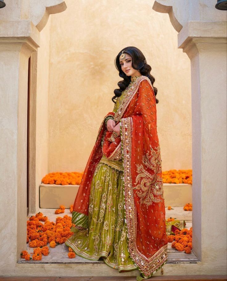 a woman in an orange and green lehenga is posing for the camera with her hands on her hips