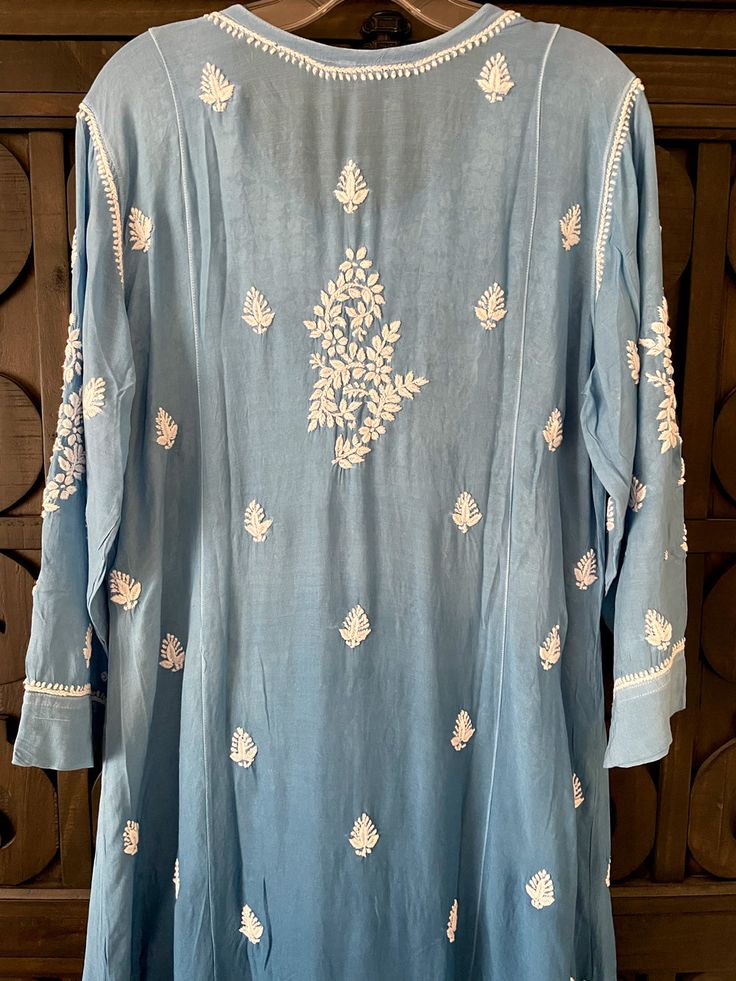 This Blue Ombre Muslin Silk Handcrafted Lucknowi Chikankari A Line Kurta Long Dress is a stunning piece of art. The beautiful blue shade dress is perfect for any special occasion. The luxurious fabric and intricate Lucknowi Chikankari embroidery make it a timeless piece that will never go out of style. Length 48" inches Long sleeves 18" inches Round neck A line Muslin silk Chikankari work Hand embroidered Dry Clean Fit: True to sizeInside Margin: NoTouch and Feel: Soft and ComfortableDispatched Traditional Light Blue Festive Dress, Light Blue Anarkali Dress With Intricate Embroidery, Light Blue Embroidered Dress For Eid, Summer Chanderi Dress With Cutdana Detail, Summer Cutdana Chanderi Dress, Bohemian Dresses With Chikankari Embroidery For Transitional Season, Transitional Long Dress With Chikankari Embroidery, Traditional Summer Dress With Cutdana, Traditional Light Blue Floral Embroidered Dress