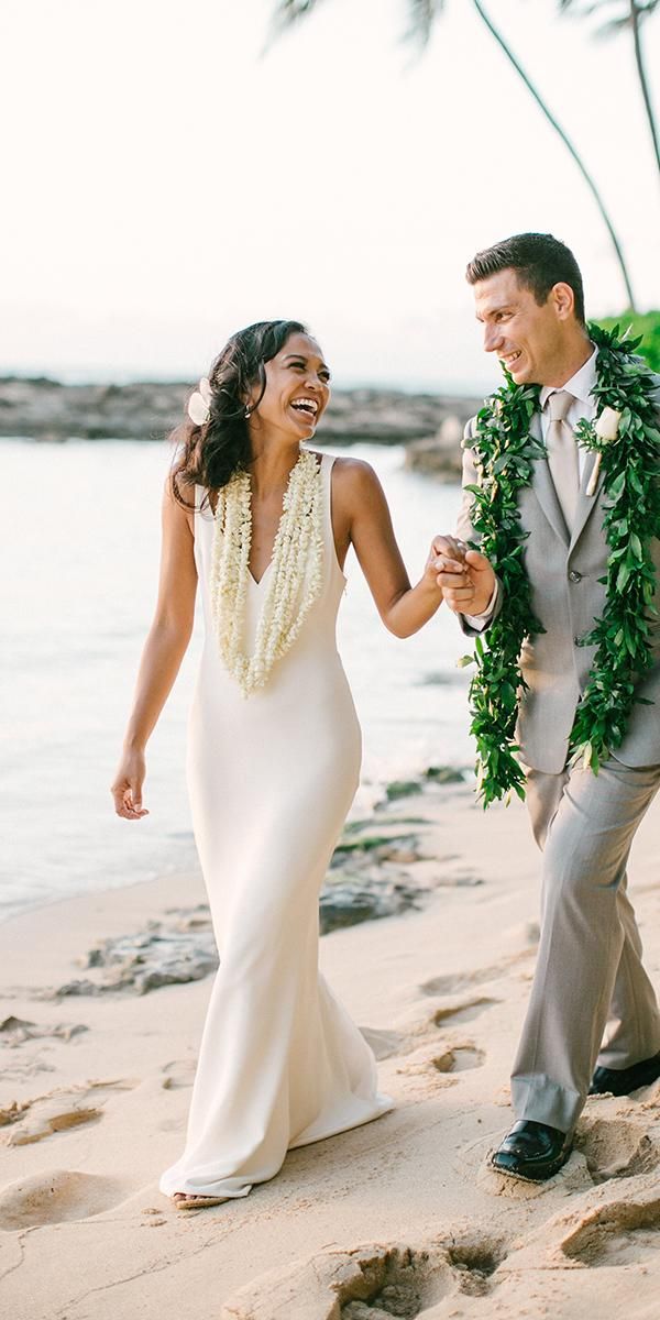 a bride and groom walking on the beach with leis around their necks in front of palm trees