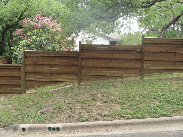 a wooden fence in the middle of a grassy area next to a street and trees