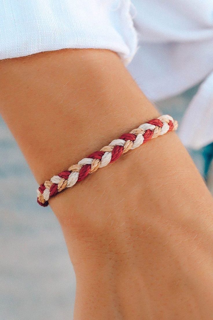 a woman's hand wearing a red and white braid bracelet on her left wrist