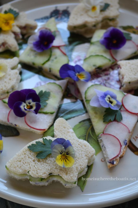 a white plate topped with sandwiches covered in cucumber and purple pansy flowers