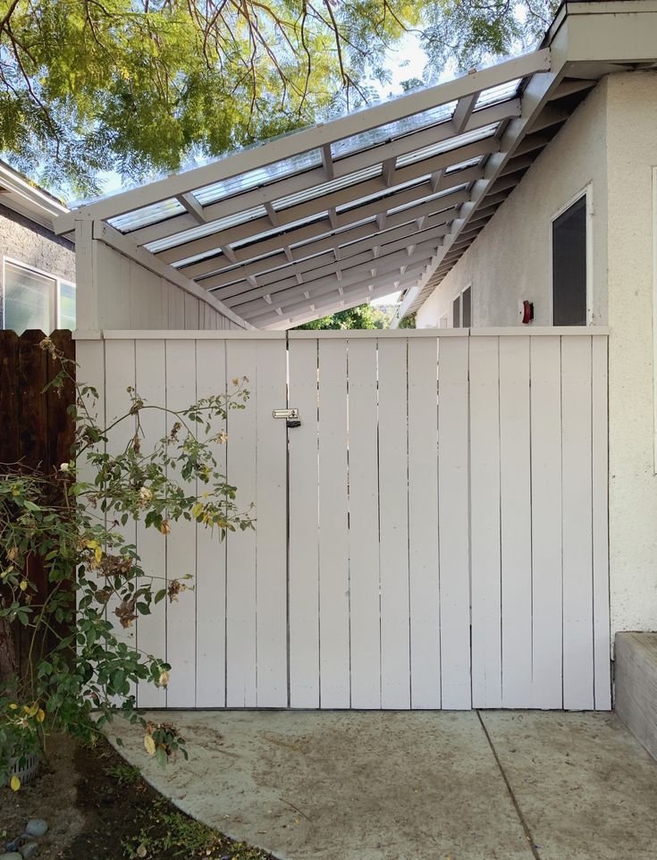 a white fence that is next to a house with a tree in front of it