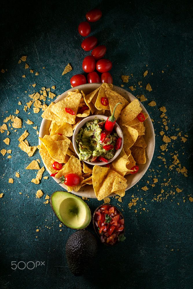 a plate with chips, tomatoes and guacamole next to an avocado