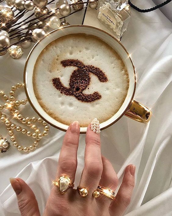 a woman's hand holding a coffee cup with chandelier decorations