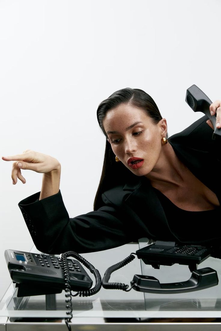 a woman sitting at a desk with a phone in her hand and pointing to the side