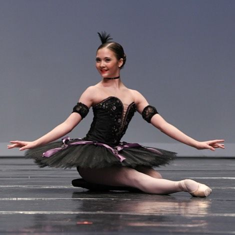 a young ballerina is sitting on the floor with her arms out and legs crossed