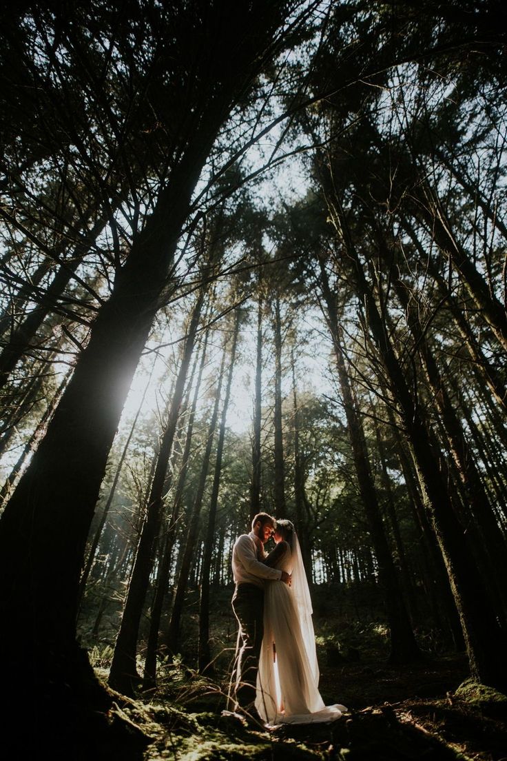 a bride and groom standing in the middle of a forest with their arms around each other