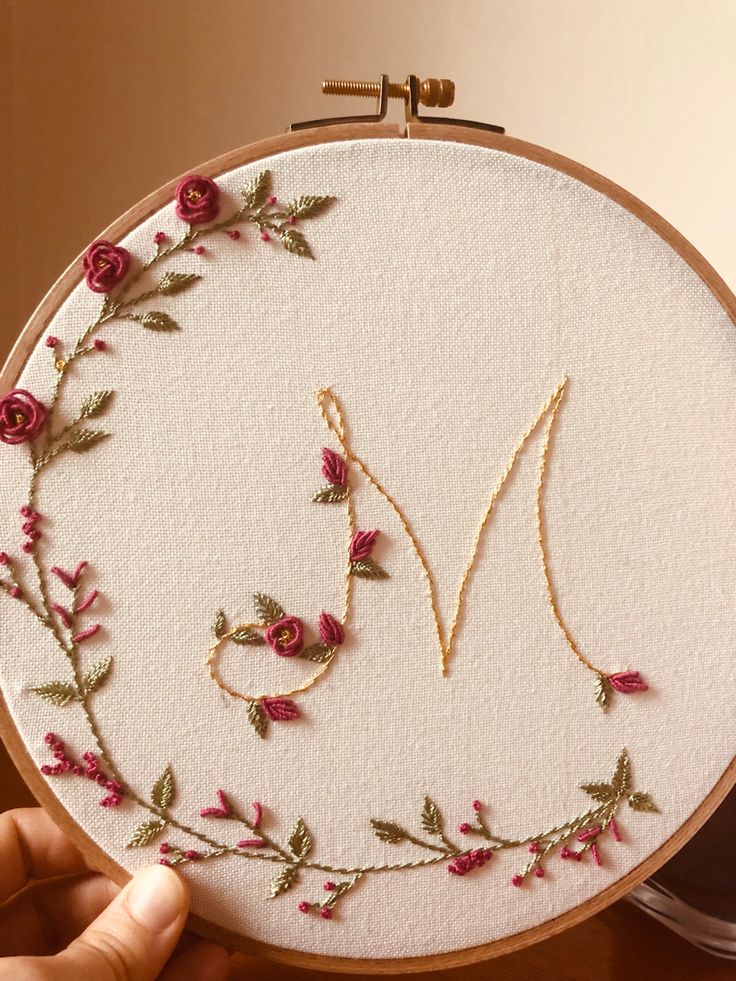 someone is holding up a embroidery hoop with the letter m in it and flowers on it