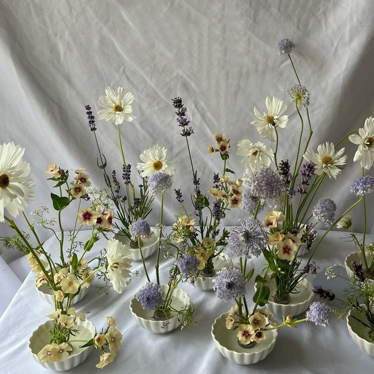 several vases filled with different types of flowers on a white cloth covered tablecloth