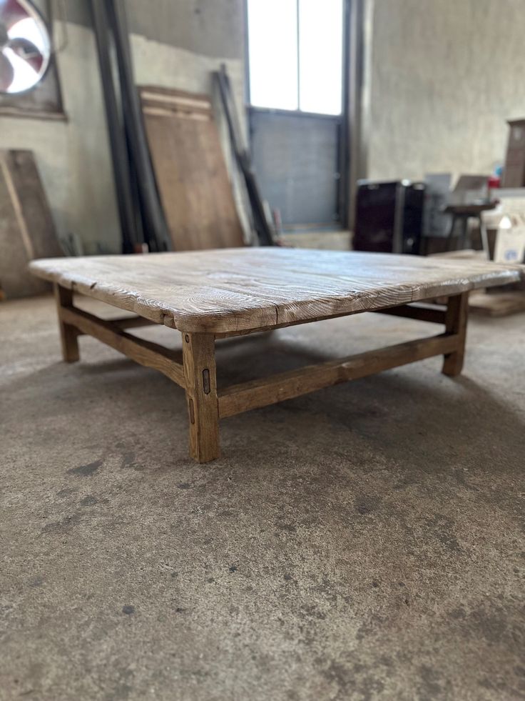 an old wooden coffee table sitting on top of a cement floor in front of a window