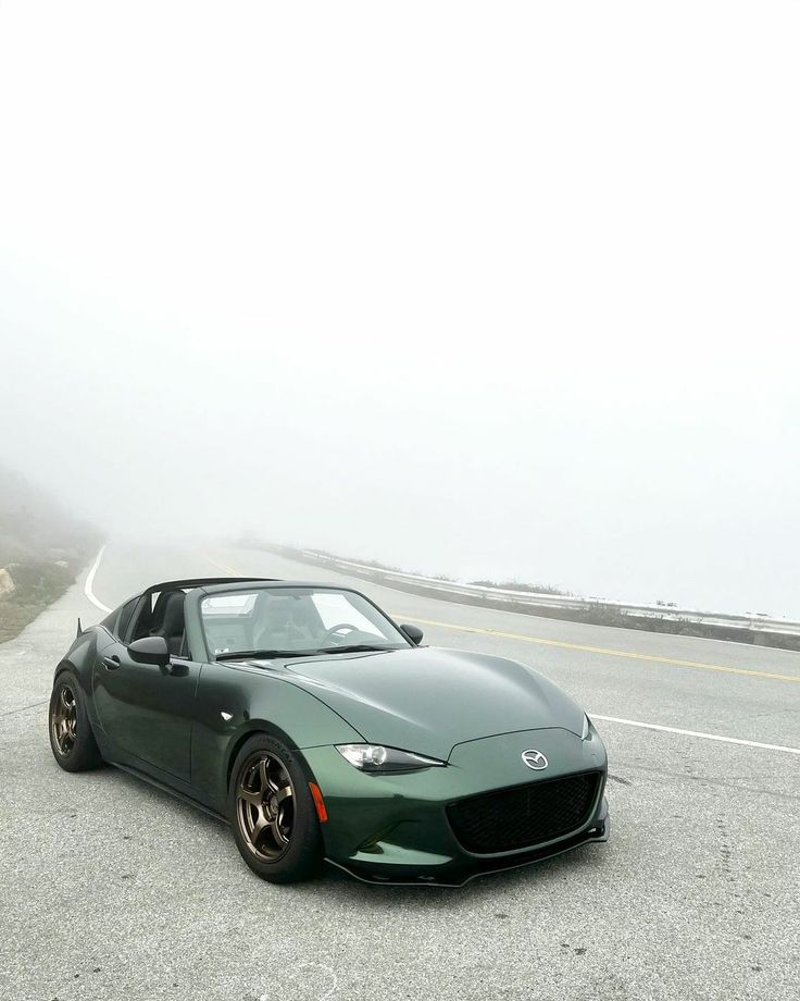 a green sports car parked on the side of the road in front of a foggy sky