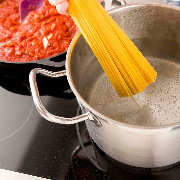 a person stirring spaghetti into a sauce in a pan on top of a stovetop