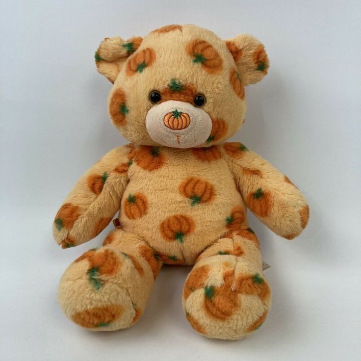 a brown teddy bear with orange pumpkins on it's face and eyes, sitting in front of a white background