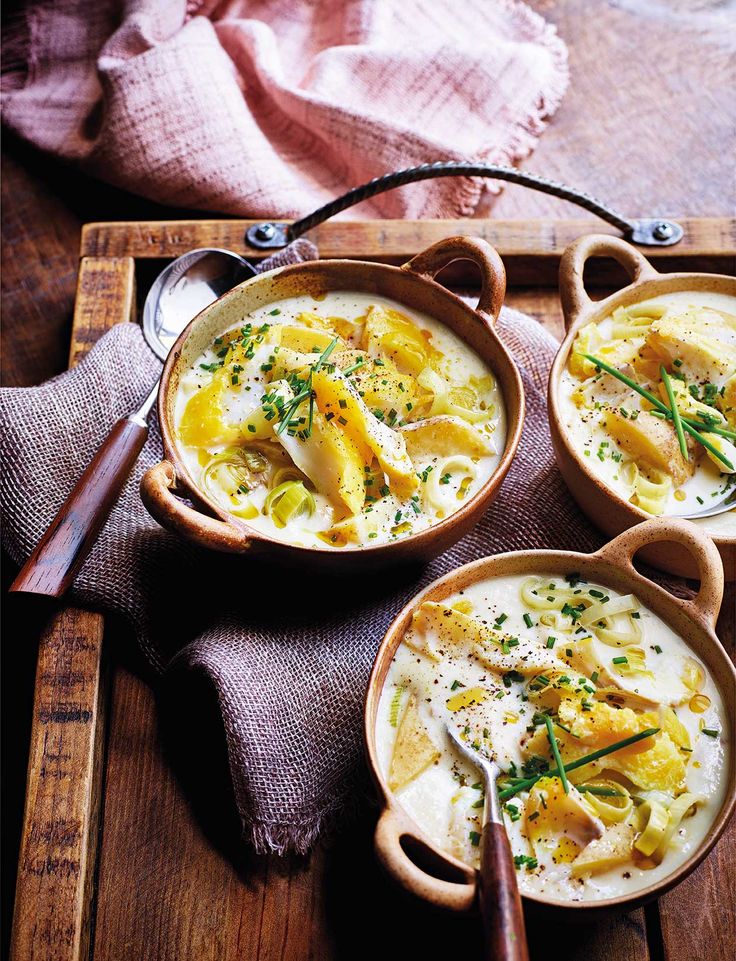 three bowls filled with soup on top of a wooden tray next to a spoon and napkin