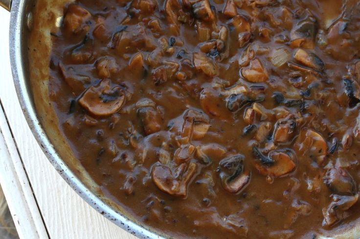 a pan filled with mushrooms and sauce on top of a wooden table