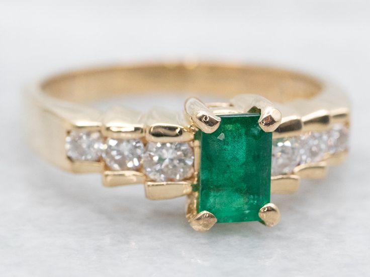 an emerald and diamond ring on a white surface