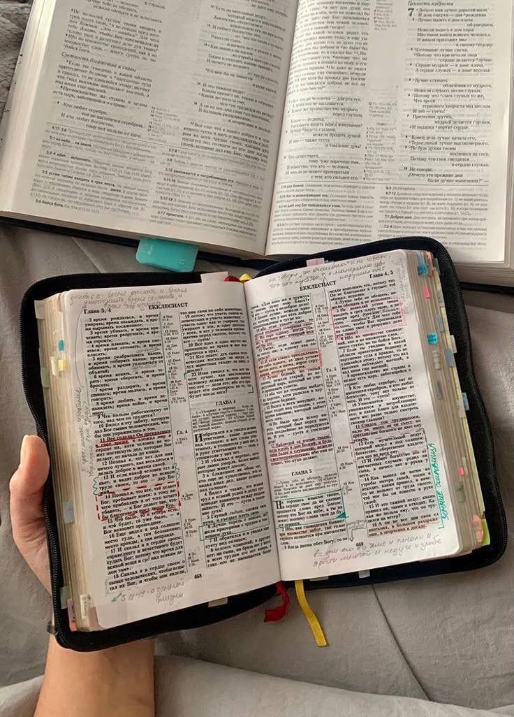 two open bibles sitting on top of a bed in someone's hand,