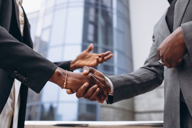 two men shaking hands in front of a tall building with glass windows and skyscrapers behind them