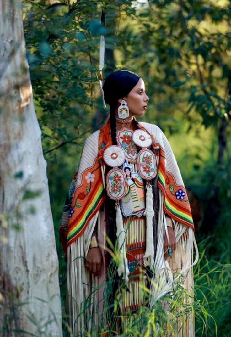 a native american woman standing next to a tree