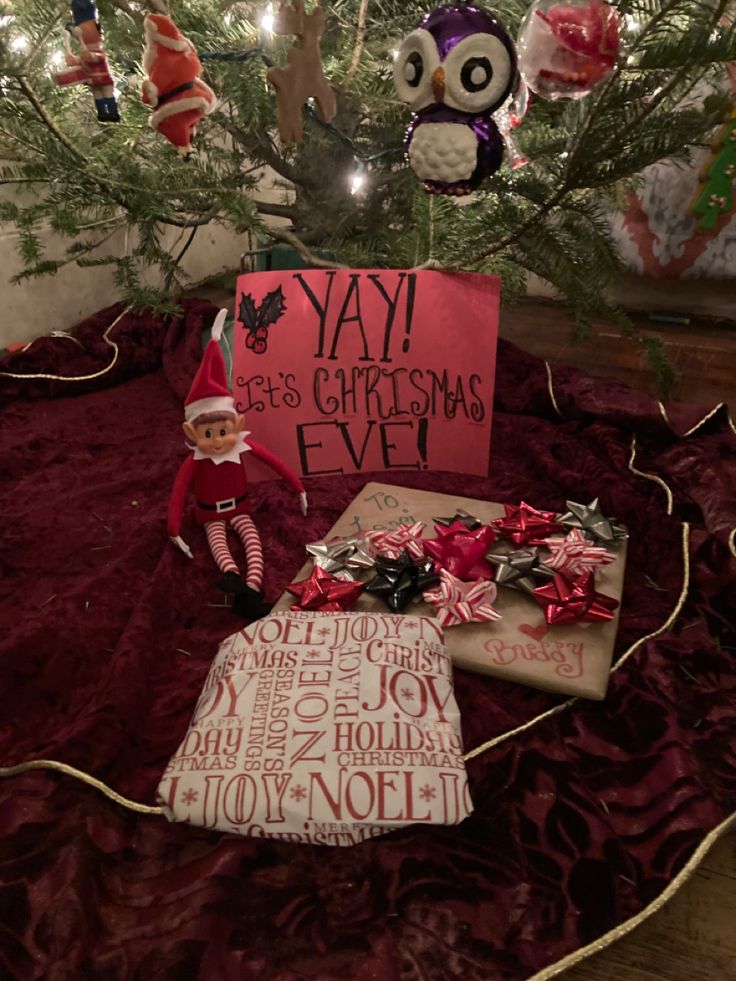 an elf is sitting in front of a christmas tree with presents under it and a sign that says yay its christmas eve