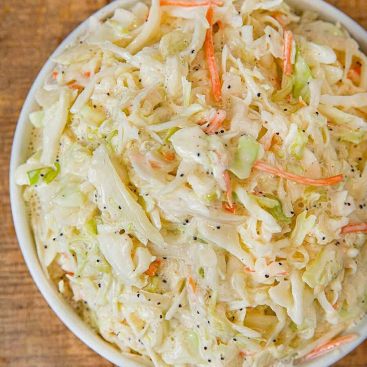 a white bowl filled with coleslaw and carrots on top of a wooden table