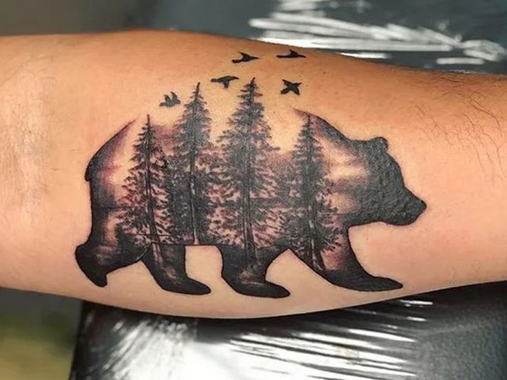 a bear with trees and birds on it's back arm, in the shape of a forest