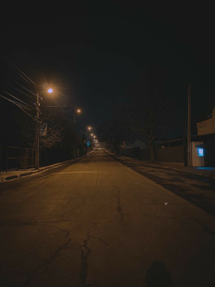 an empty road at night with street lights and no cars on the side or in front of it