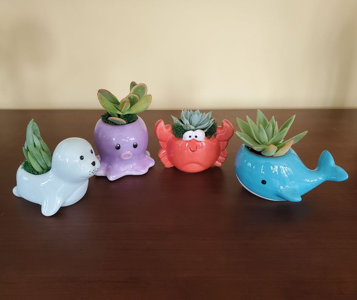 four ceramic sea animals with succulents and plants in their mouths on a table