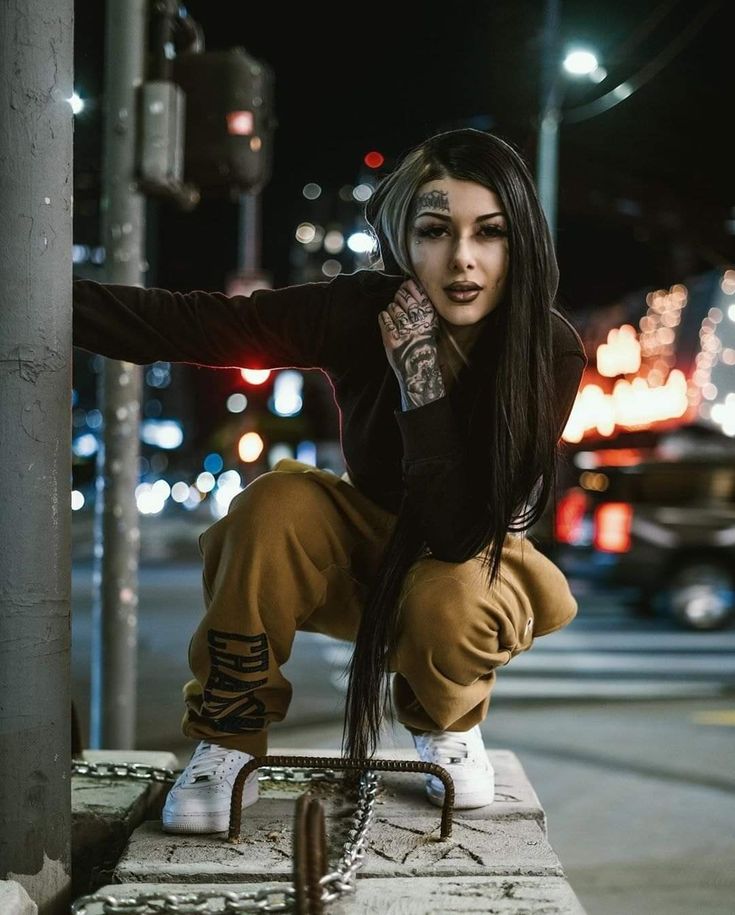 a woman with long hair and piercings sitting on a curb next to a pole