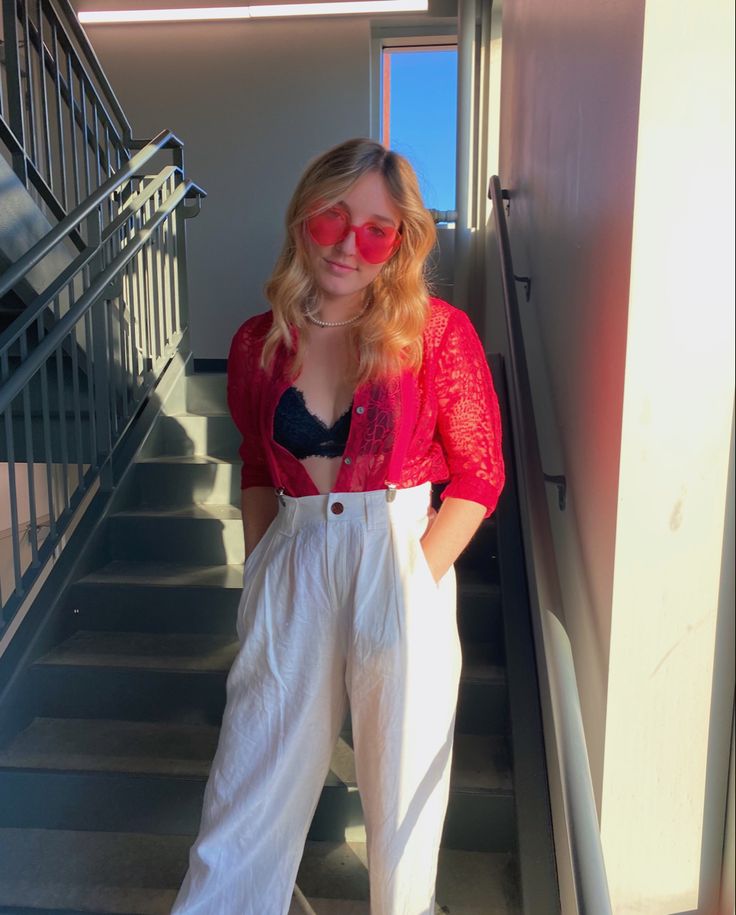 a woman in red shirt and white pants standing at the bottom of stairs with her hands on her hips