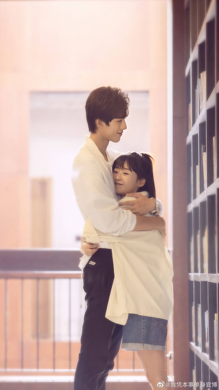 a man and woman embracing each other in front of a bookcase