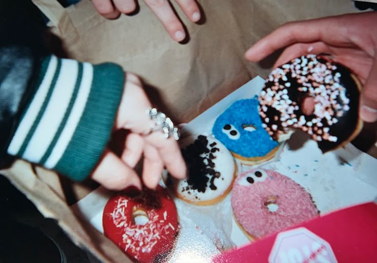 two people grabbing doughnuts from a box with sprinkles on them