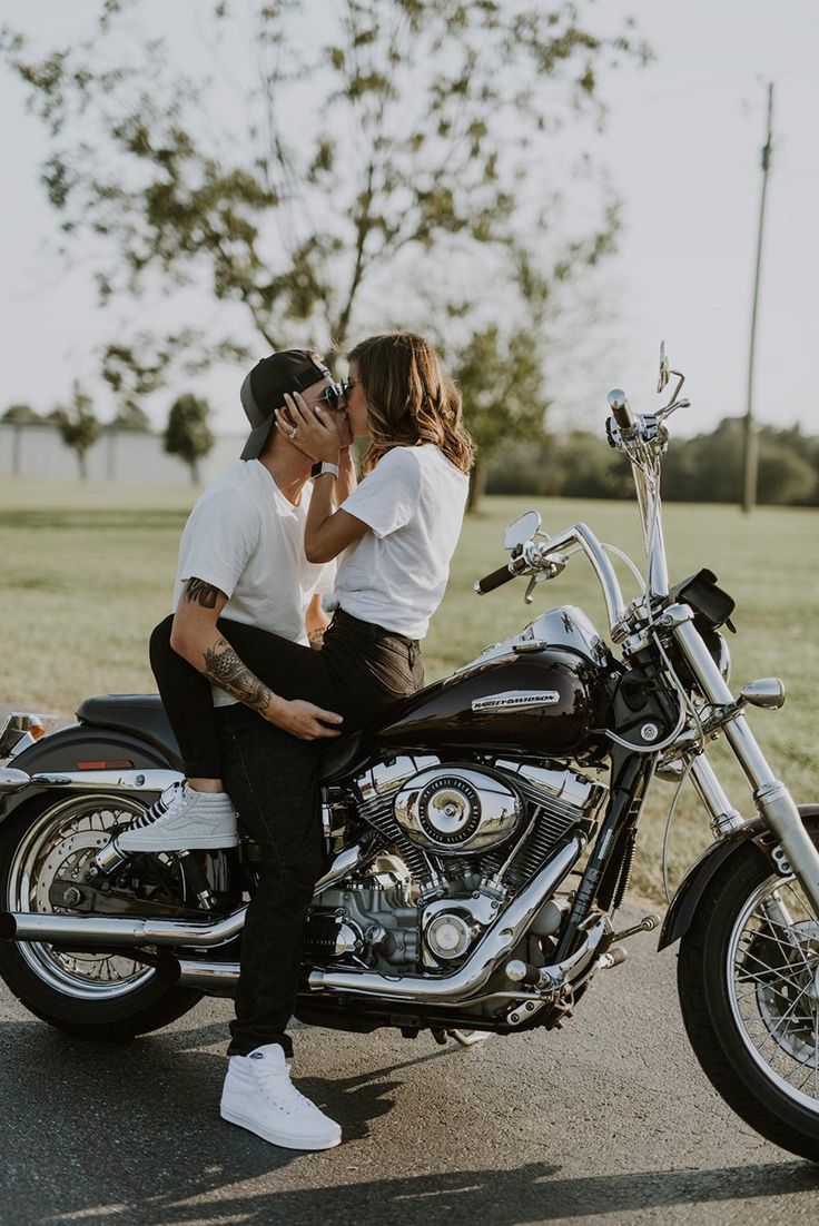 a man and woman kissing on the back of a motorcycle